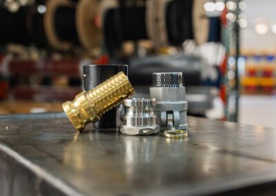 Metal camlock fittings and hose connectors, shown on a workbench at PT Hose & Bearing.