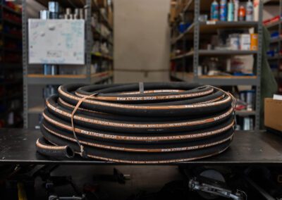 A coiled hydraulic suction and return hose sits on a metal surface at PT Hose & Bearing.